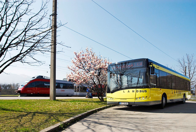 Foto eines fahrenden gelben Busses neben einem fahrenden rot-weißen Zug