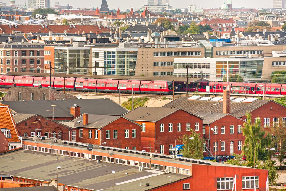 Aerial von zwei roten Zügen der DSB an einem Bahnhof zwischen Häusern in Kopenhagen.