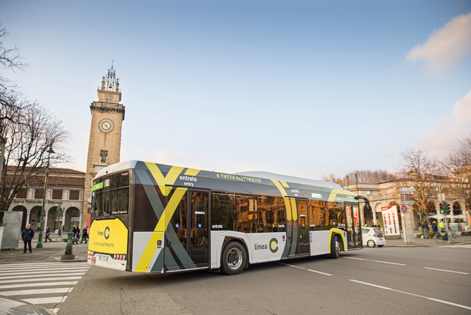Bergamo von oben mit vielen Hausdächern sowie einer befahrenen, von Bäumen gesäumten Straße.