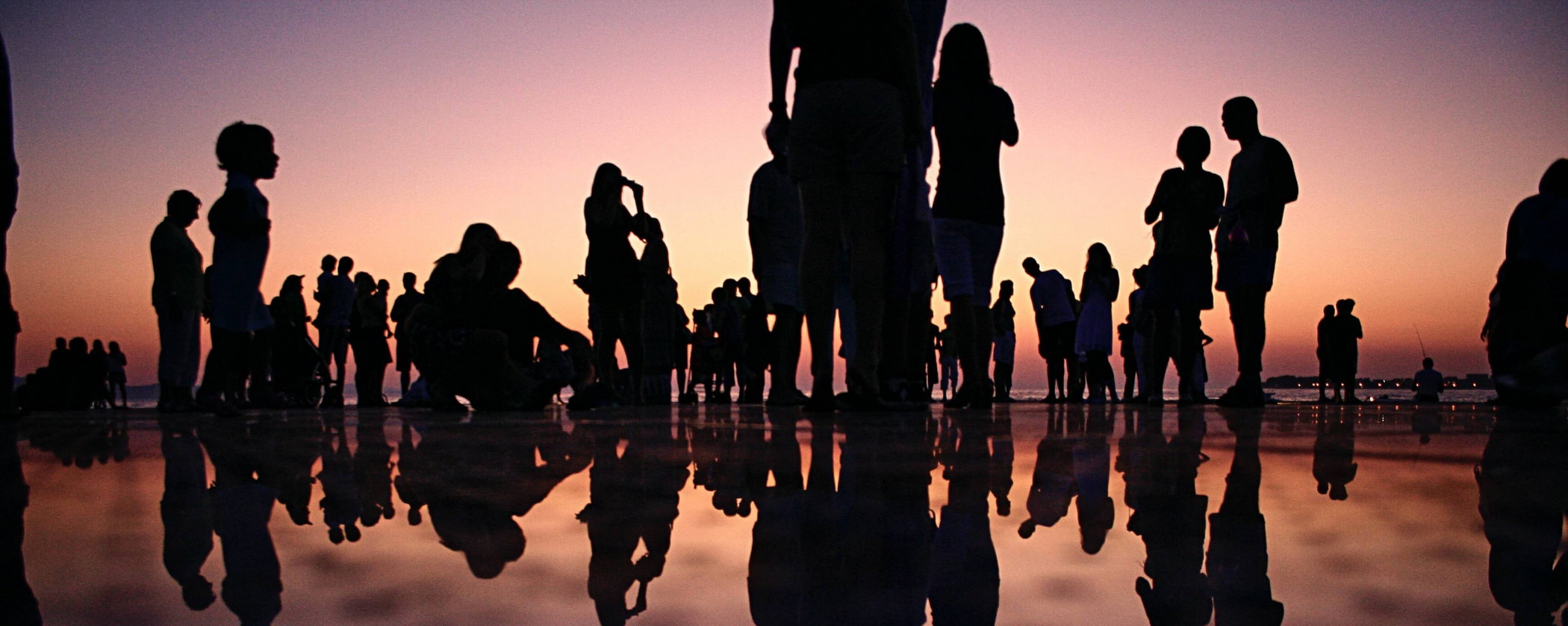 Schwarze Silhoutten von Menschen am Wasser bei Sonnenuntergang