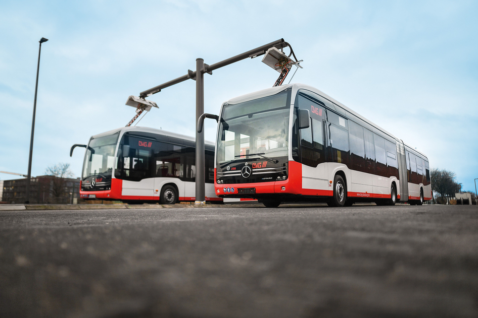 Zwei rot-weiße Elektrobusse von EvoBus werden an einer Ladesäule auf einem Betriebshof geladen.