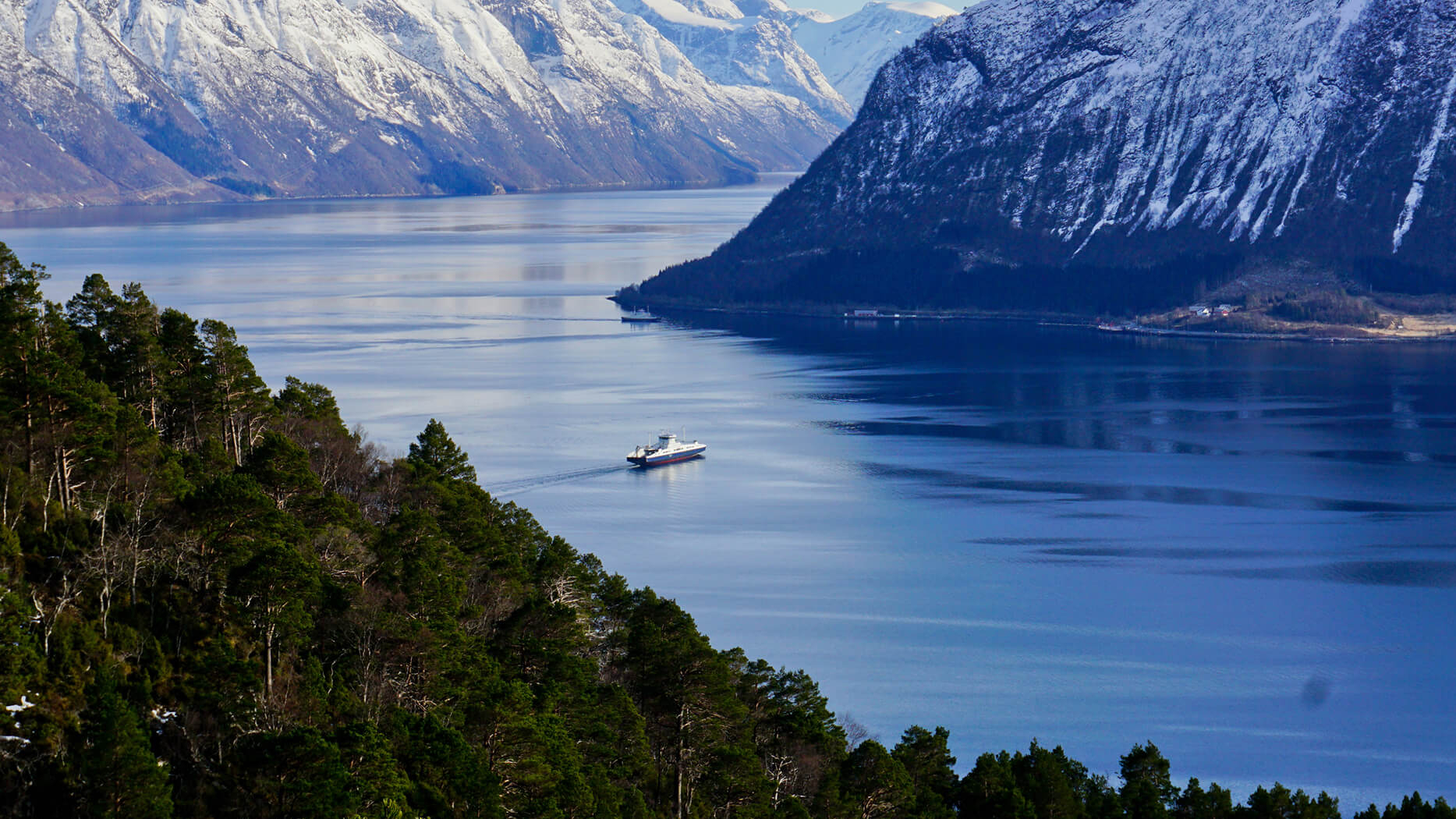 Fähre auf Fluss zwischen Schneebergen und Wald in Norwegen