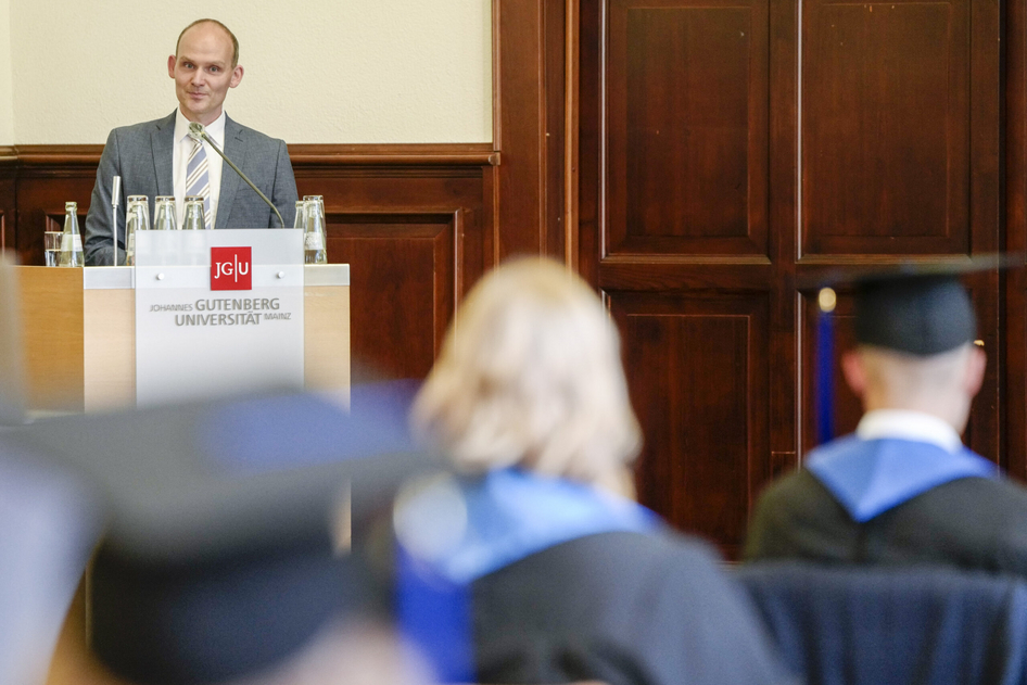 Dr. Falko Hagebölling hält eine Rede vor Absolventen in einem Hörsaal.