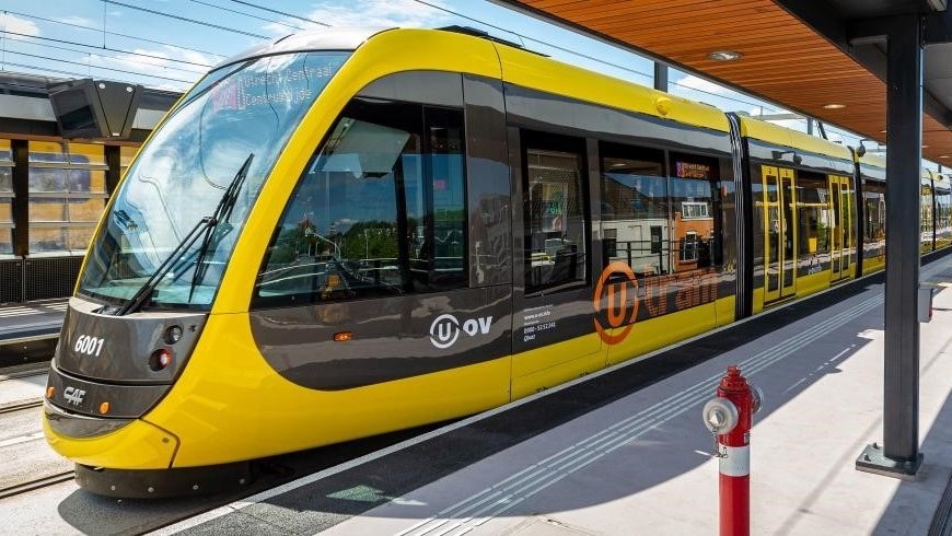 Eine gelb-schwarze Straßenbahn der Provinz Utrecht steht an einer Station.